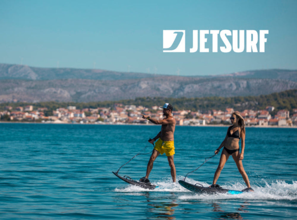 Two people jetsurfing on a clear day with a cityscape in the background, featuring the Jetsurf logo.